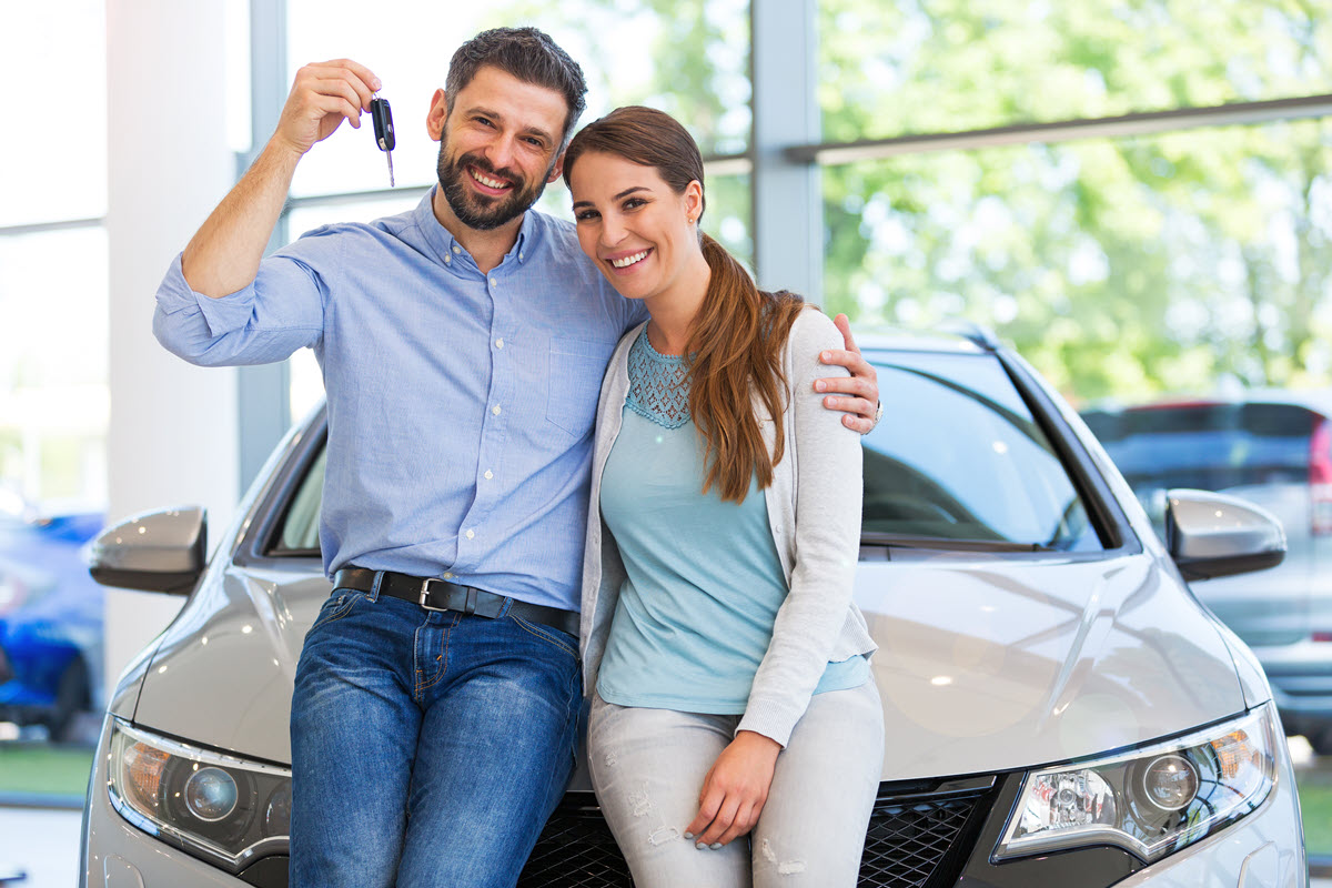couple holding keys to a car leaning on a car